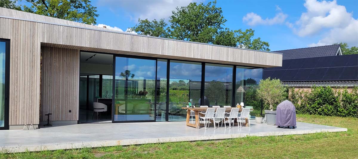 Gevlinderd betonterras met naadloze overgang naar moderne bungalow met grote glazen puien in Best